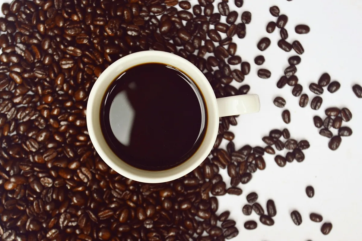 Overhead view of a white cup of black coffee surrounded by roasted coffee beans