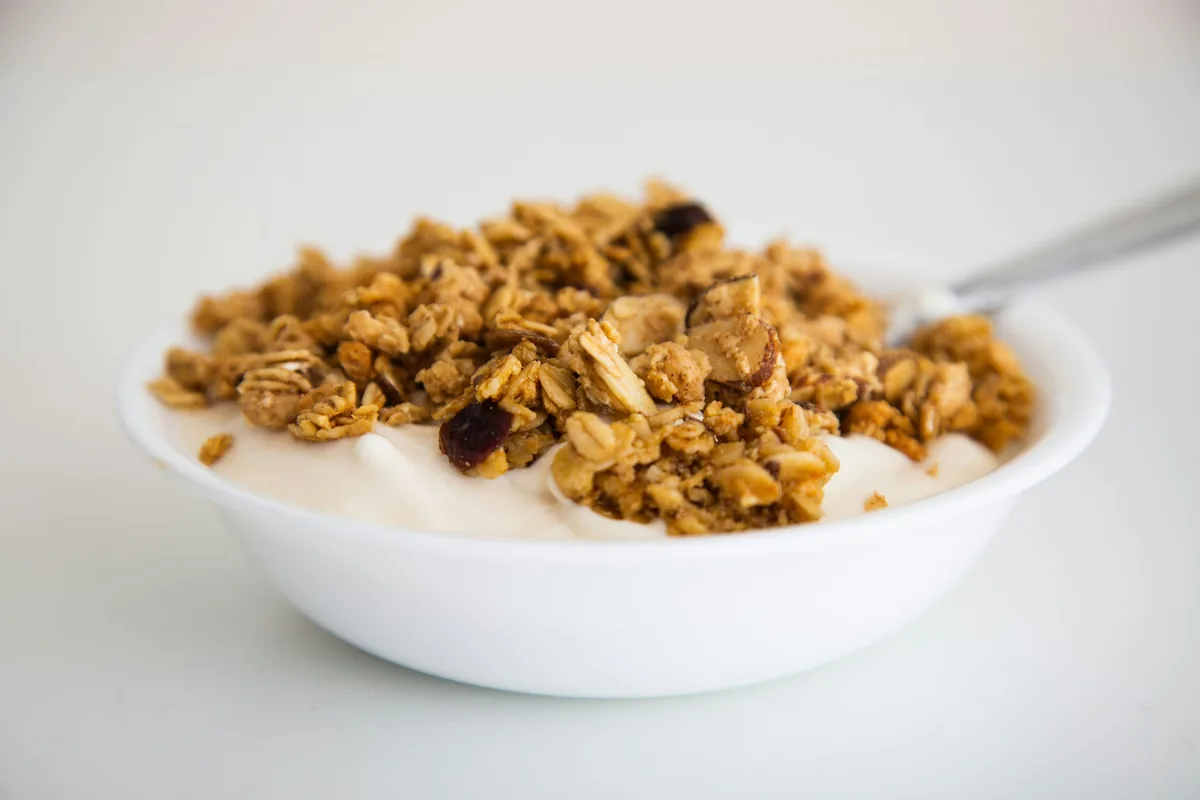 A white bowl of plain yogurt topped with granola, with a spoon