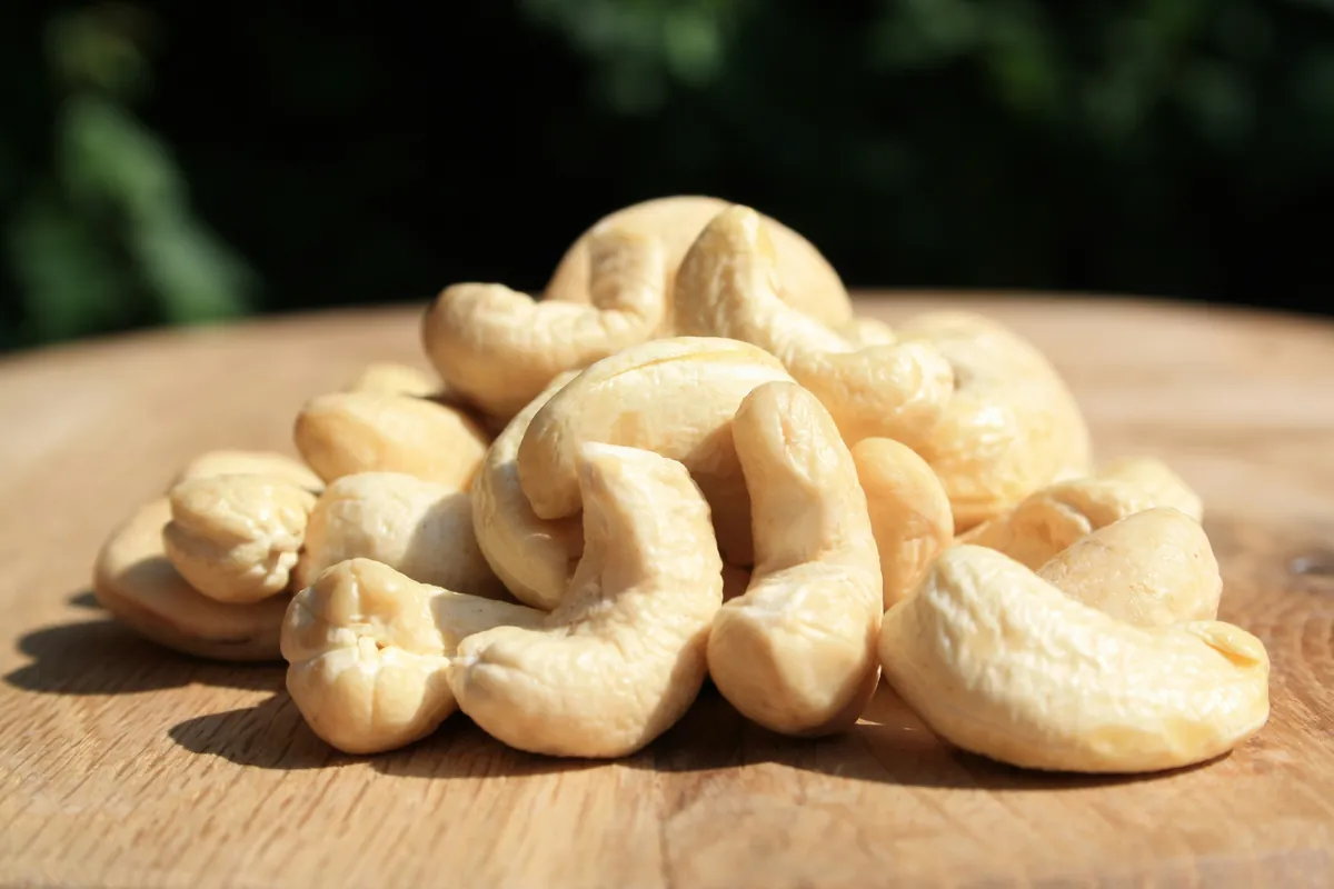 A pile of whole cashew nuts on a round wooden board in sunlight