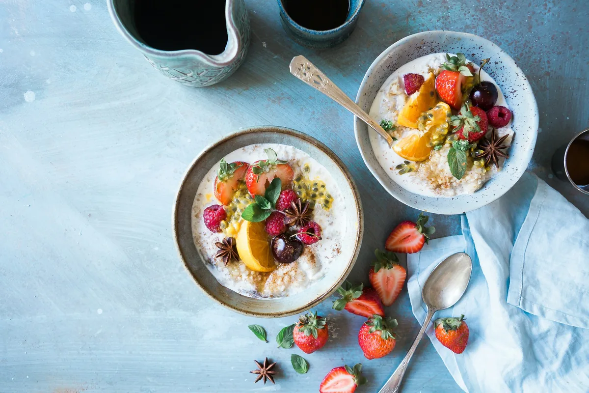 Two bowls of oatmeal topped with strawberries, raspberries, orange slices and passion fruit on a pale blue table