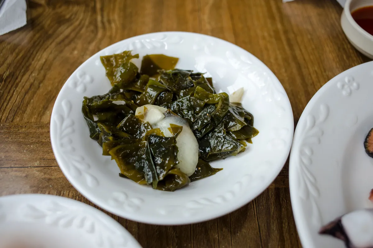 A white plate of seaweed and onion salad on a wooden table