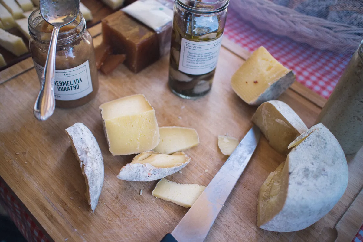 Wedges of hard cheese with a knife and jars of jam on a wooden board
