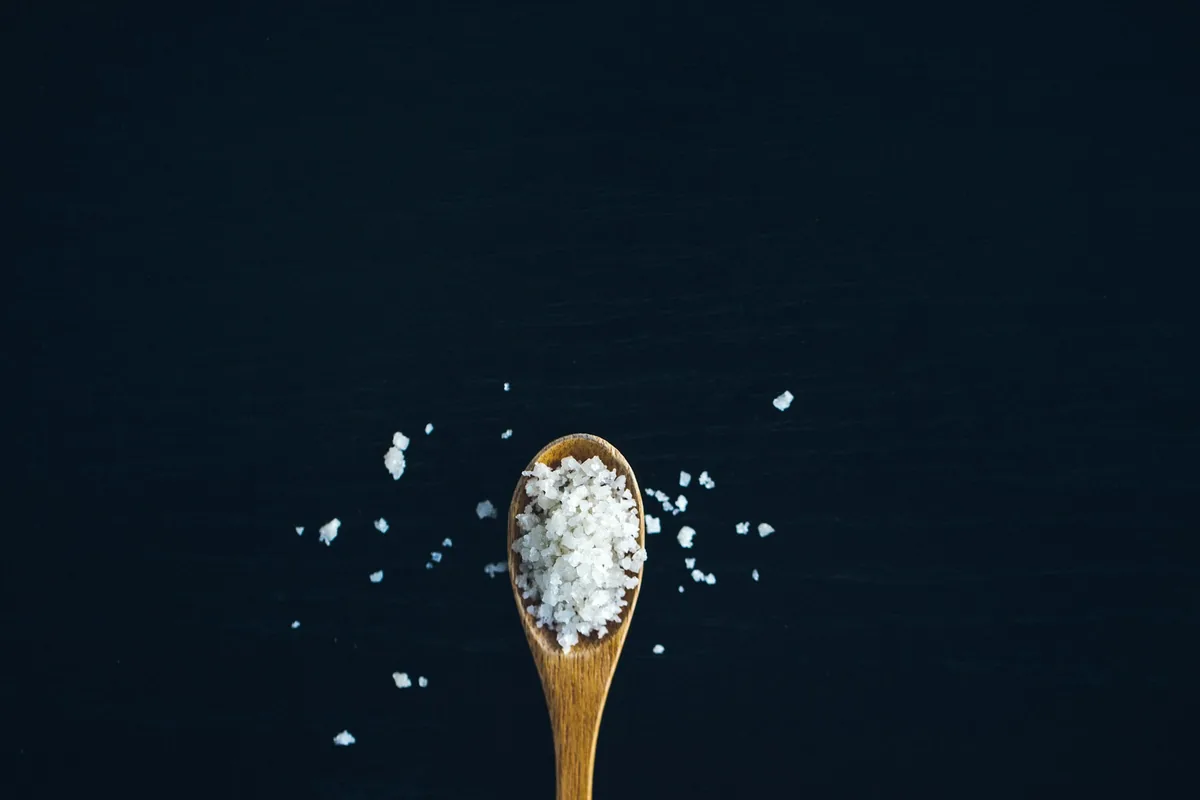 Coarse sea salt flakes on a wooden spoon against a dark background