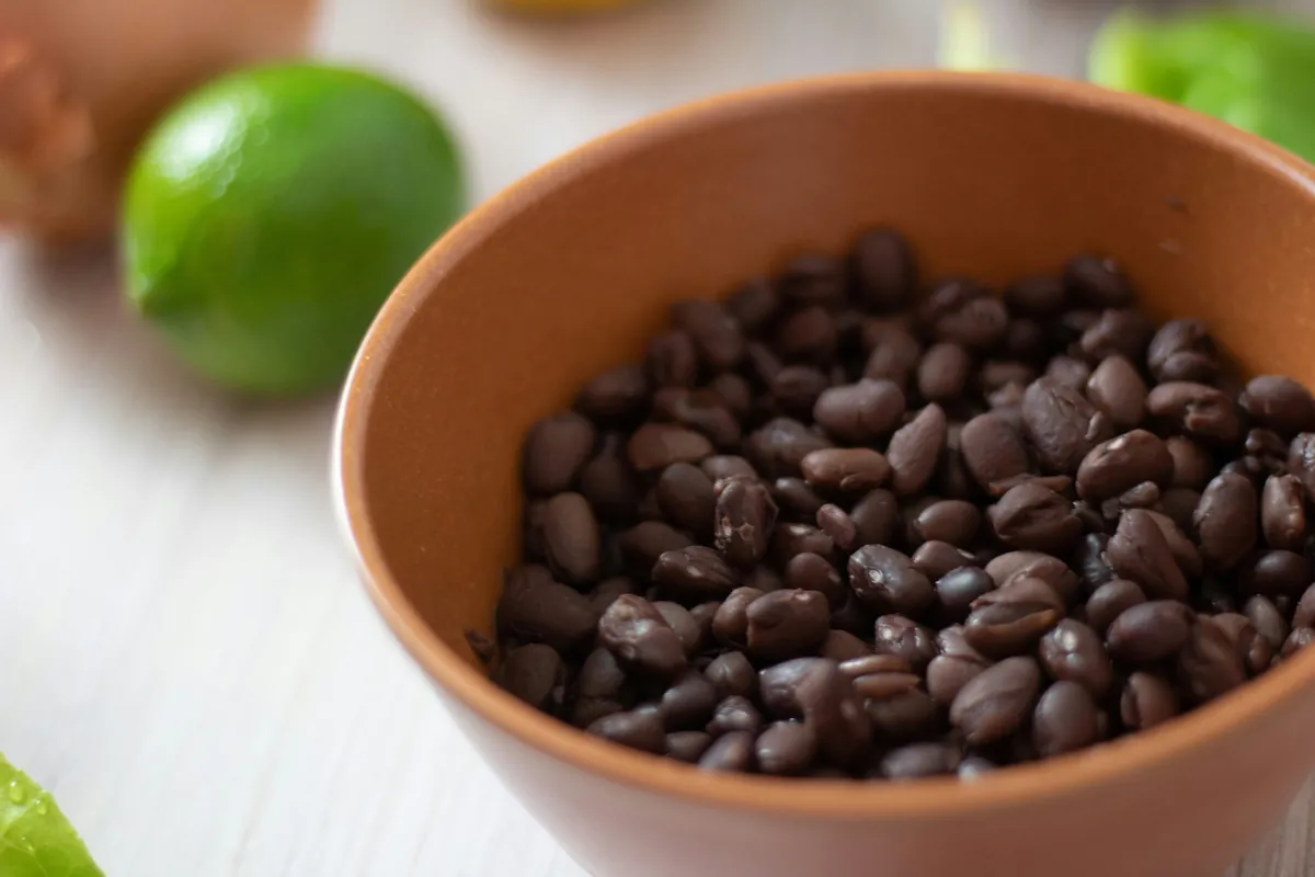 A terracotta bowl of black beans beside fresh limes