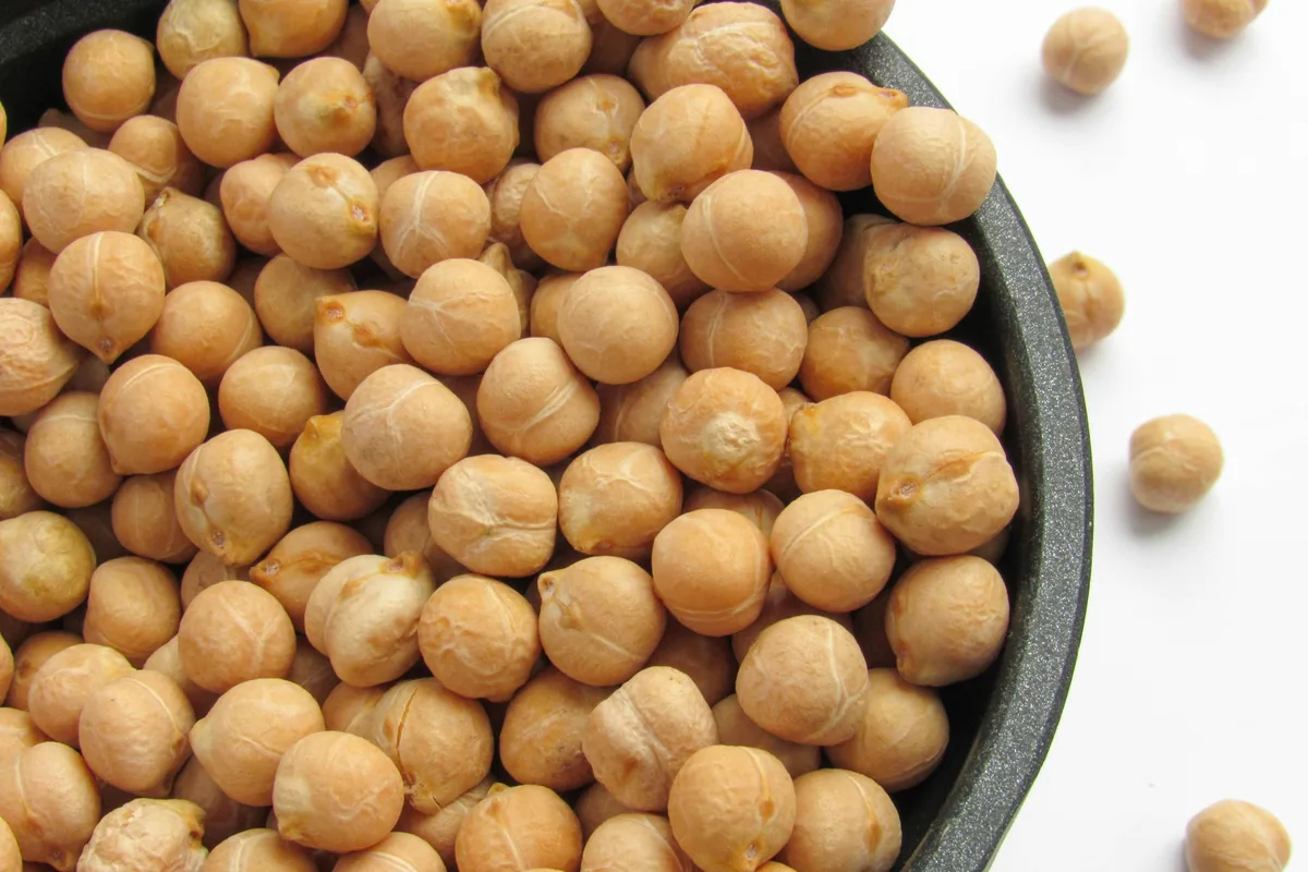Close-up of dry chickpeas piled in a dark pan with a few scattered on a white surface